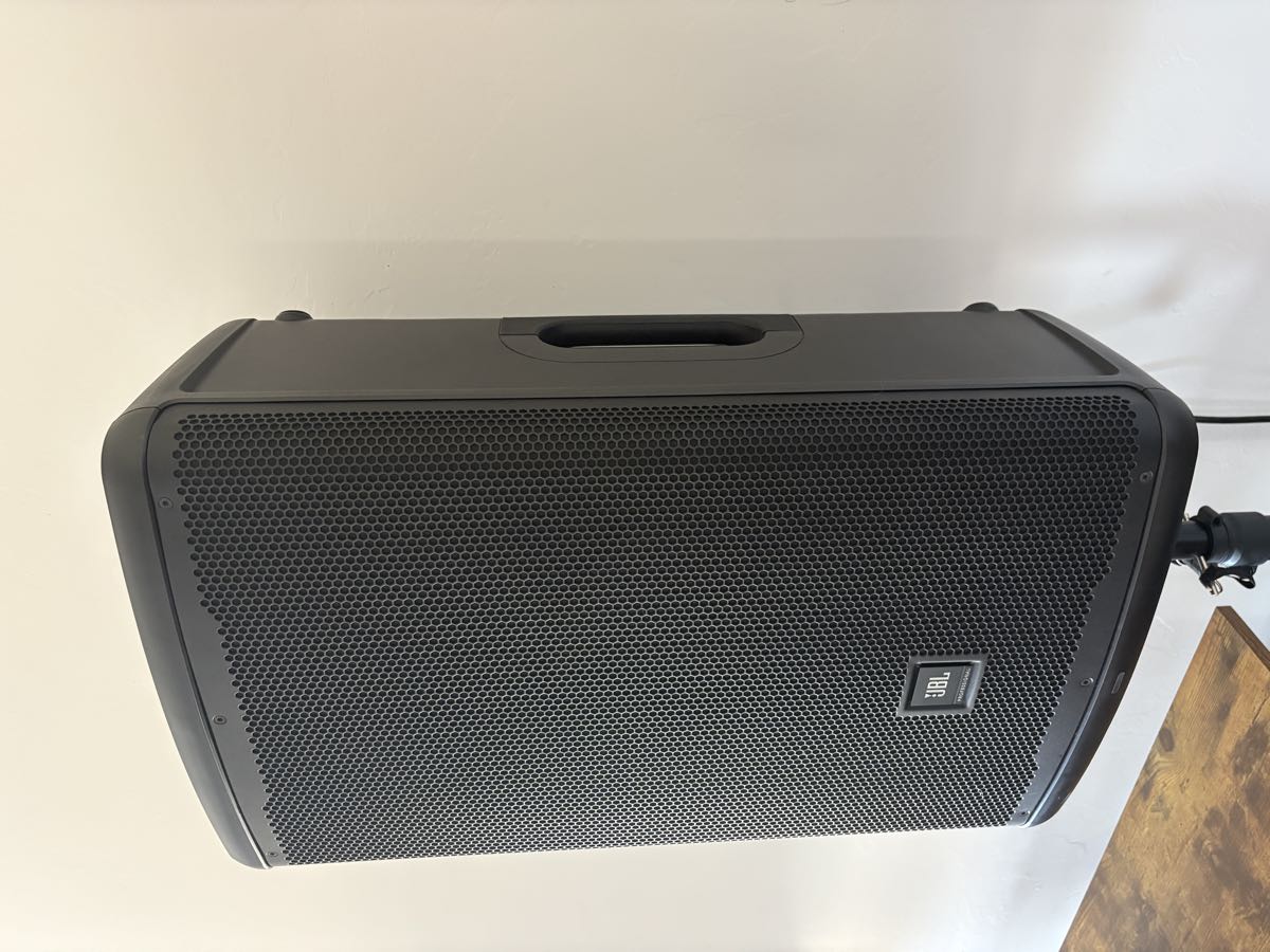 A JBL EON715 powered speaker on a stand, seen at an angle.